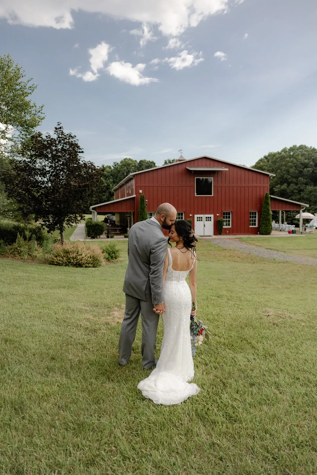 Couple embracing in front of the red barn at The Heritage Barn wedding venue in Conover, NC