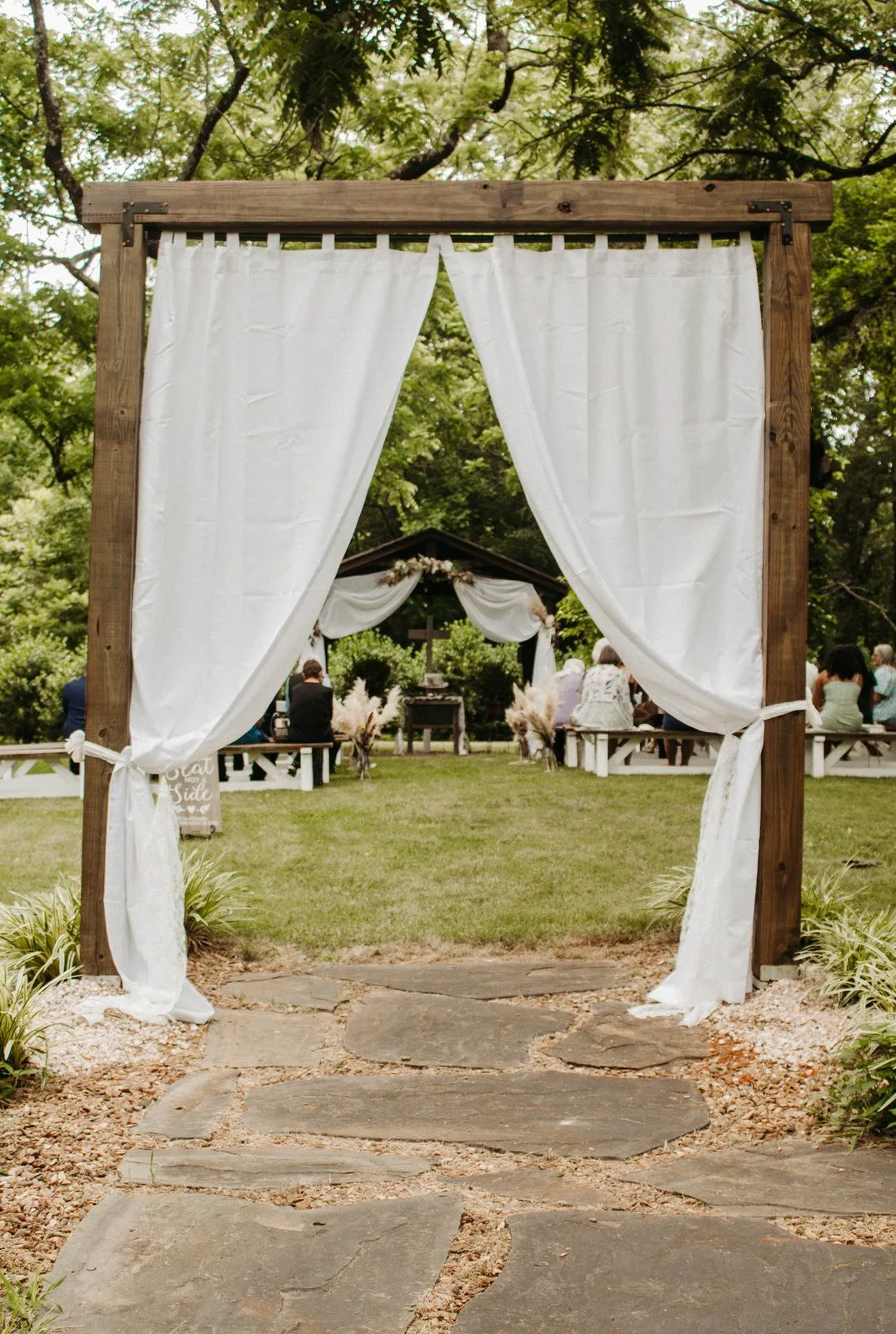 White draped ceremony arch set among the trees at The Heritage Barn outdoor ceremony site