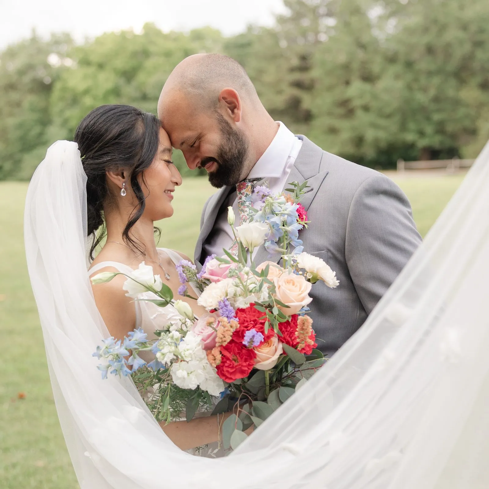 Couple embracing with a vibrant bouquet and a swirling veil at The Heritage Barn