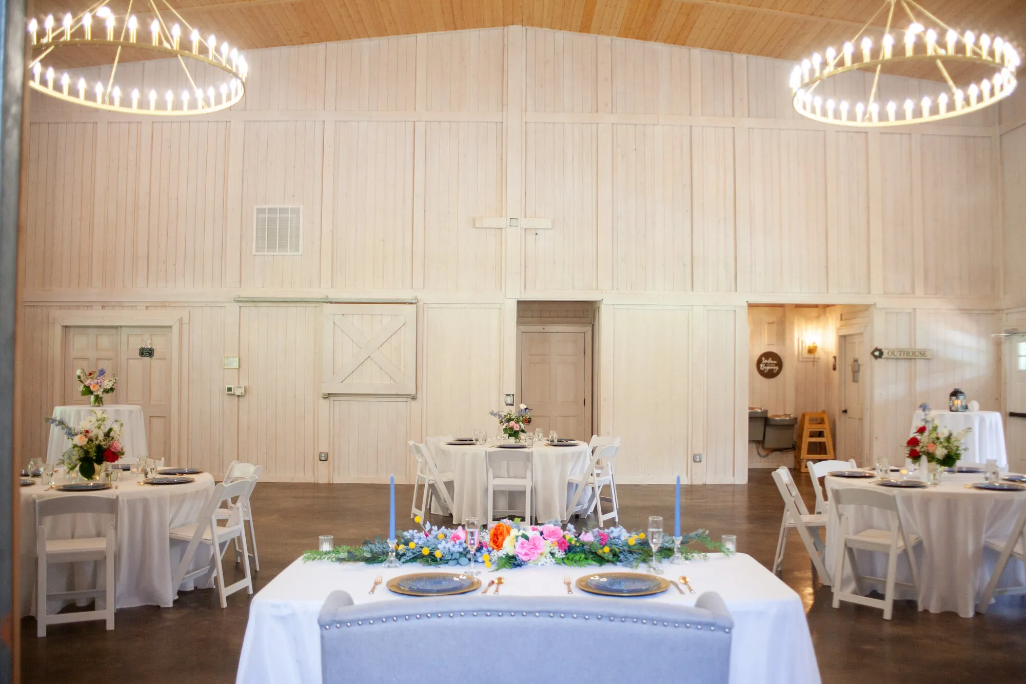 Reception head table beneath chandeliers inside the barn at The Heritage Barn