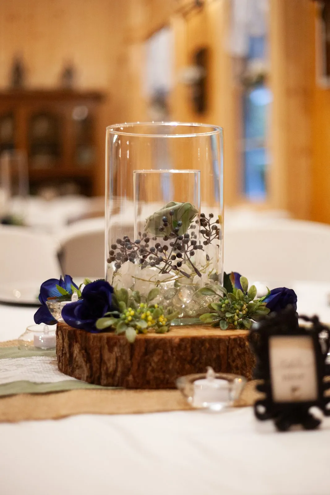 Tablescape detail with a hurricane candle and florals on a wood slice at The Heritage Barn