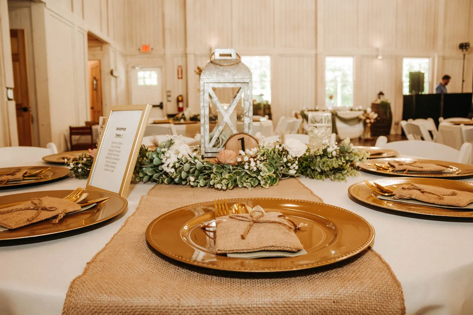 Elegant place setting with gold chargers and a tall floral centerpiece at The Heritage Barn